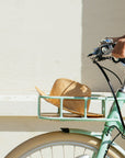 A straw hat sits in the front rack of a Bluejay e-bike in Mint Green