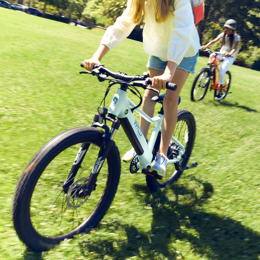 A girl riding a Bluejay WILD Kids' e-bike in Mint Green.