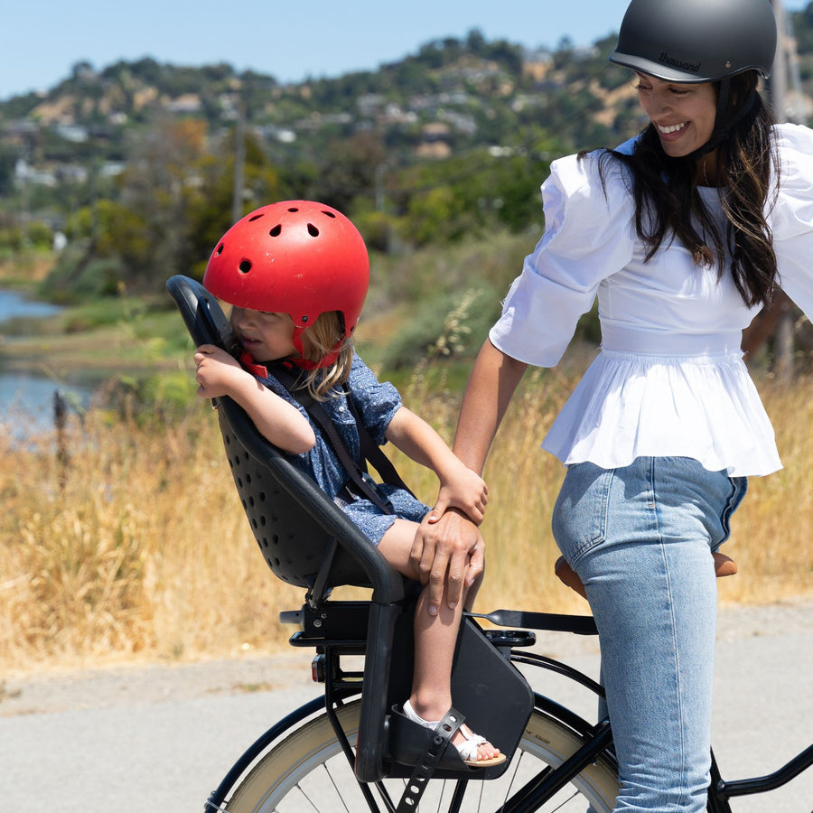 A woman smiles at her child while sitting on a Bluejay e-bike in Classic Black with a rear child seat. 