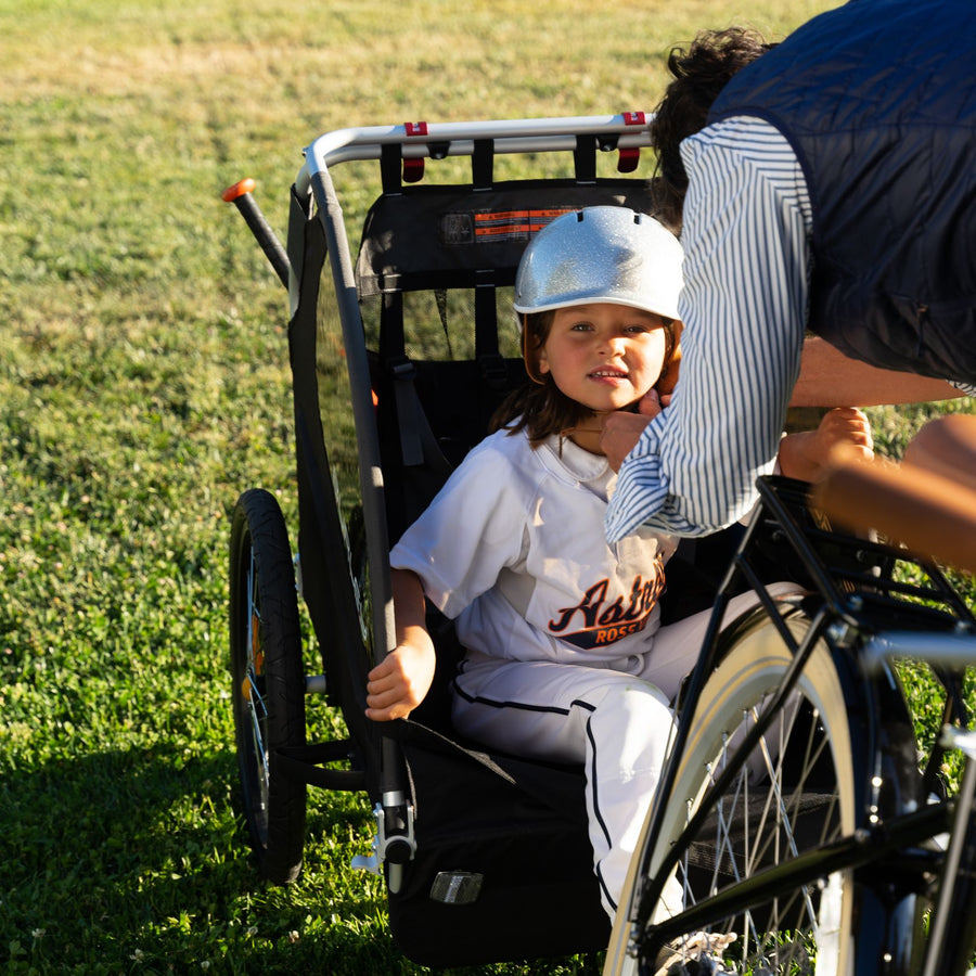 A mother straps her child into a Burley bike trailer behind a Bluejay e-bike. 