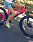 A girl rides a Bluejay WILD kids' e-bike in Hot Pink