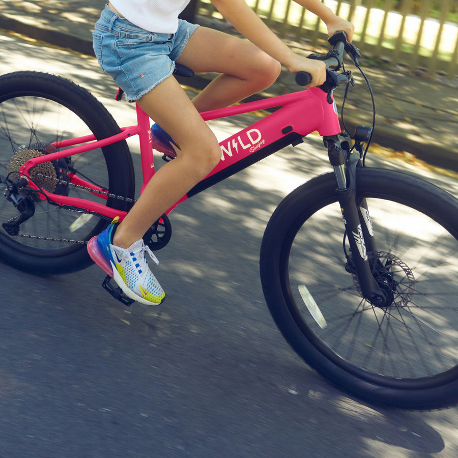 A girl rides a Bluejay WILD kids' e-bike in Hot Pink