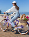 Woman riding Bluejay Premiere Edition e-bike in French Lavender with rear Bolga basket