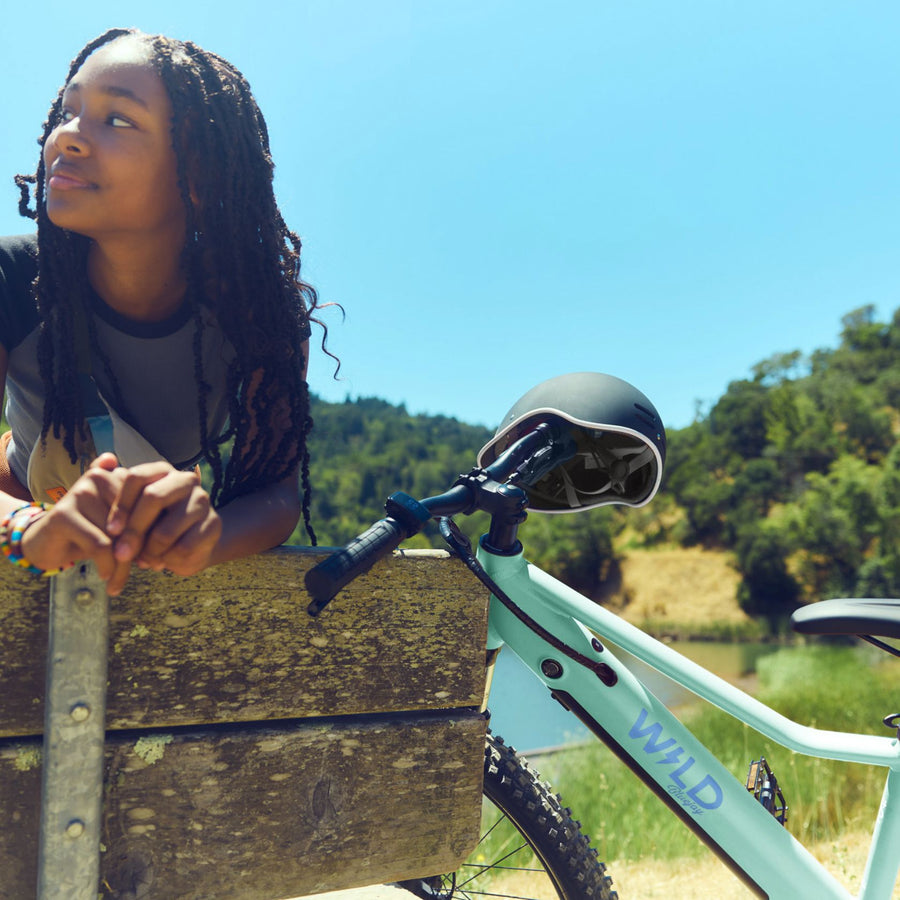 A girl sitting next to a Bluejay WILD kids' e-bike in Mint Green.