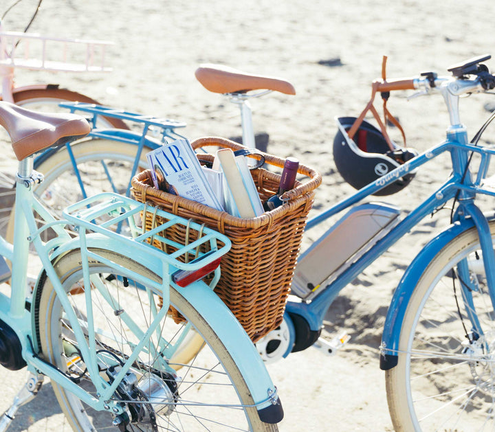 Bluejay Premiere Edition e-bikes in Mint Green and Bluejay Blue at beach with rear basket 